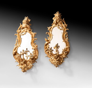 View full screen - View 1 of Lot 20. A pair of carved giltwood mirrors fitted as wall lights, probably German, circa 1750-1760 | Paire de miroirs formant appliques en bois sculpté et redoré, travail étranger, probablement allemand, vers 1750-1760.