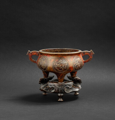 View full screen - View 1 of Lot 160. Brûle-parfum tripode en bronze avec inscriptions arabes XVIIE siècle | 十七世紀 銅阿拉伯文雙耳三足香爐 《宣德年製》仿款 | An arabic-inscribed bronze incense burner on a lotus wood stand, 17th century.
