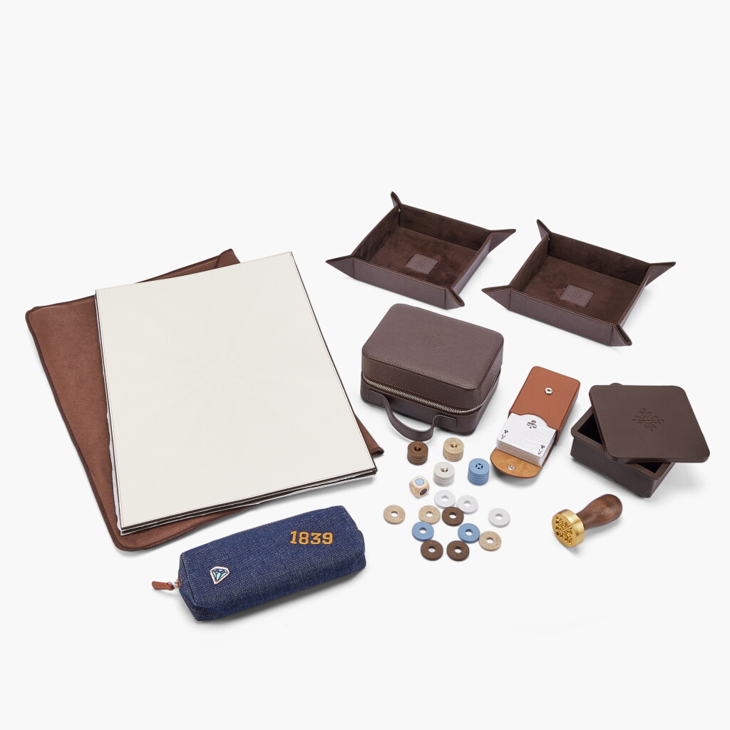 View full screen - View 1 of Lot 8687. A set of one gilt brass and wood ice cube stamp with ice cube mold, one playing card and quiz card set with chips, die and travelling case, four leather table mats, two leather valet trays and one colouring pencil set by Caran d’Ache with colouring book, Circa 2026.