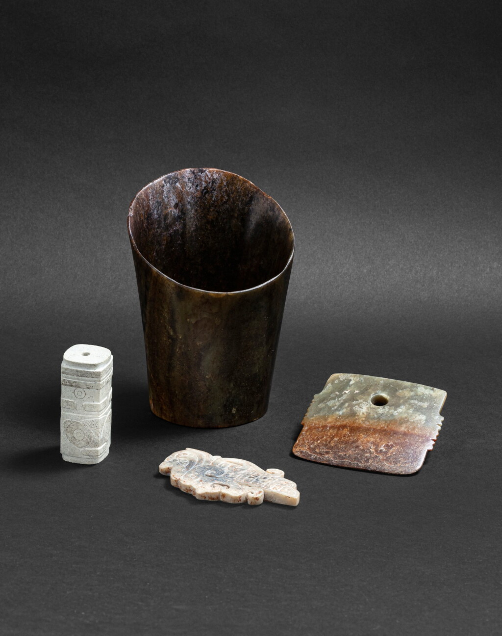 View full screen - View 1 of Lot 163. Ensemble de quatre jades archaïsants Dynastie Ming ou antérieure | 明或更早期 仿古玉器一組四件 | An archaistic hoof-shaped jade ornament, a liangzhu culture-type miniature cong, an archaistic jade ornament and an archaistic jade blade, Ming Dynasty or earlier.