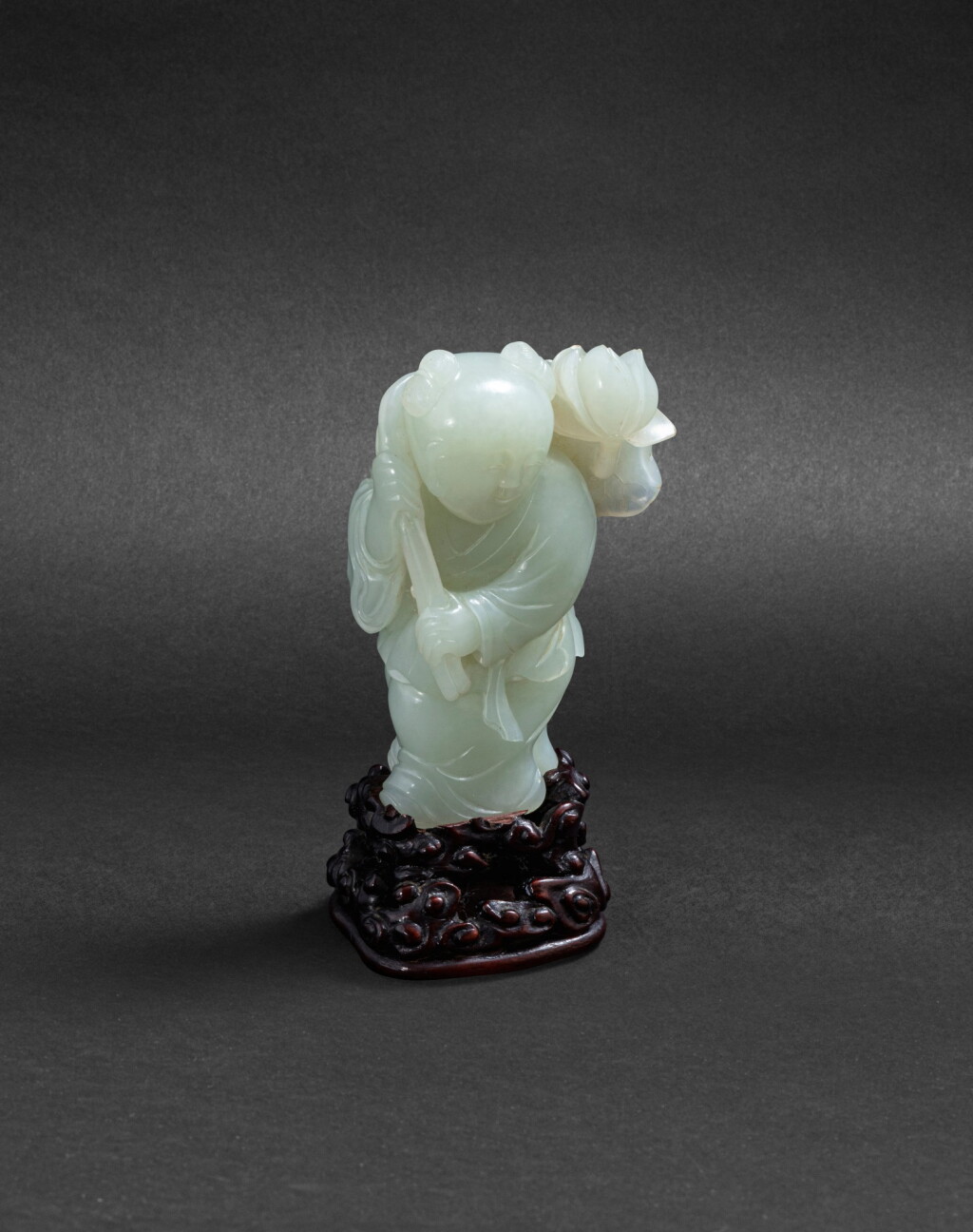 View full screen - View 1 of Lot 213. Groupe en jade céladon sculpté Fin de la Dynastie Qing | 清晚期 青白玉持蓮童子把件 | A celadon jade 'boy and lotus' carving, late Qing Dynasty.