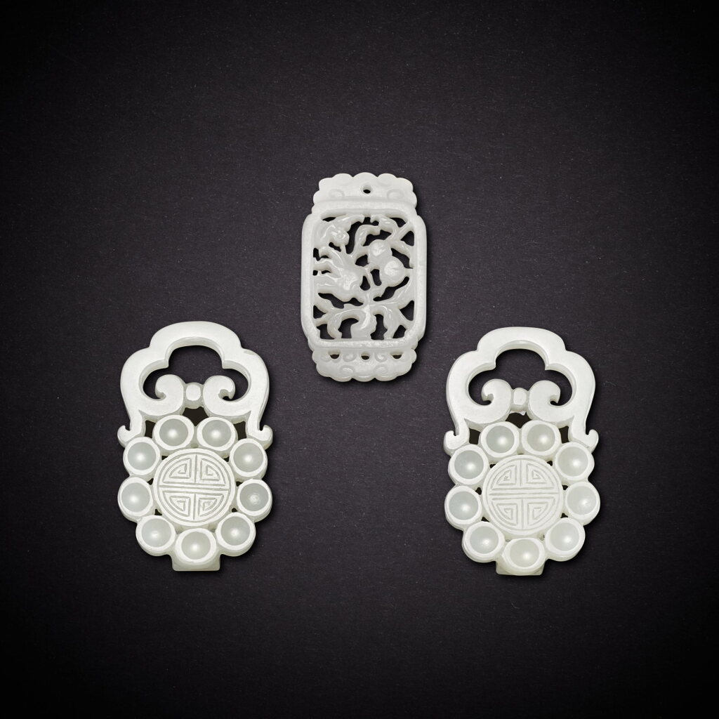 View full screen - View 1 of Lot 6936. A pair of white jade 'longevity' belt buckles and a white jade reticulated 'bat and fruits' pendant, Qing dynasty, 18th - 19th century | 清十八至十九世紀 白玉壽字帶扣一對及白玉鏤雕福壽雙全珮一件.