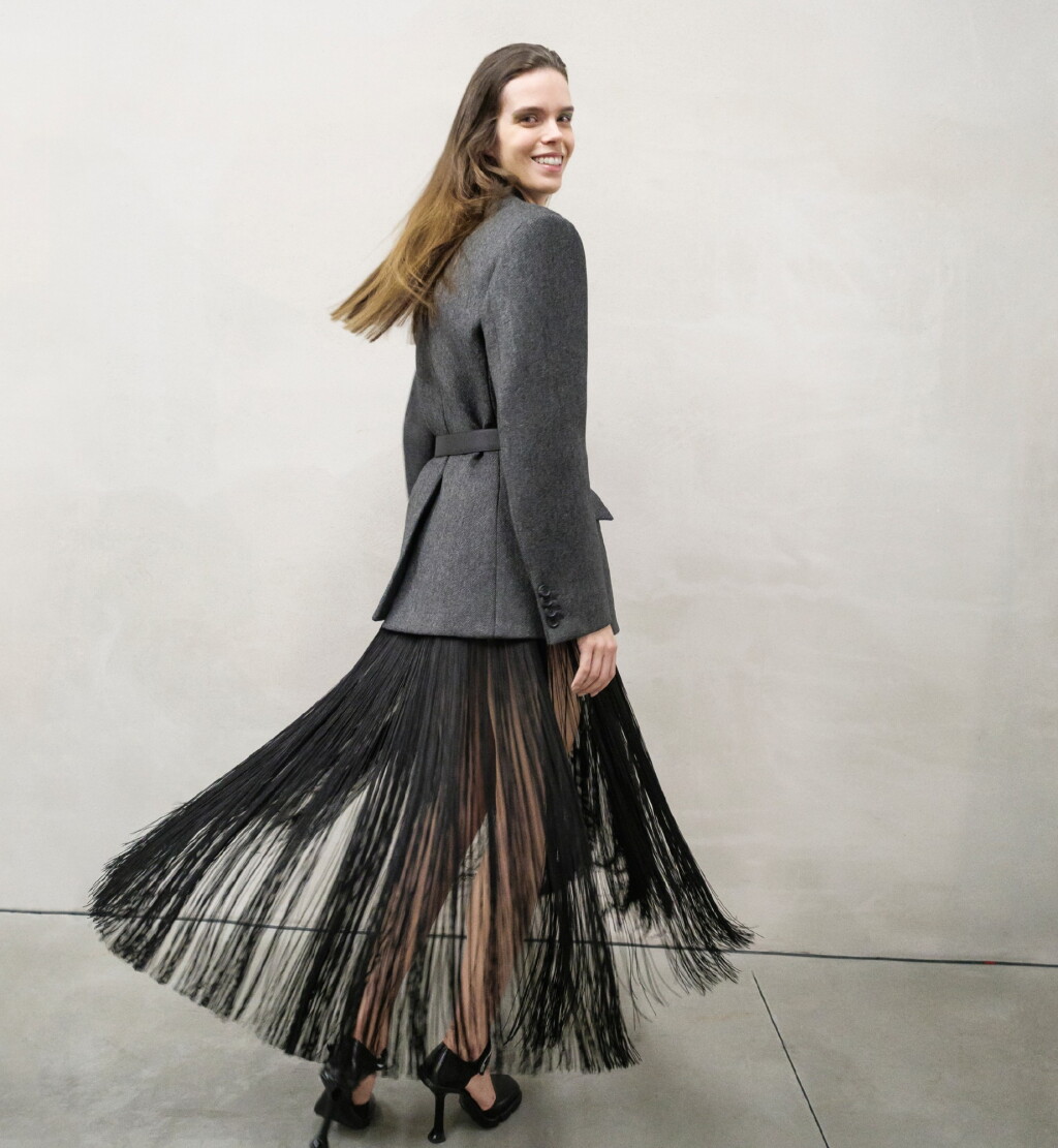 View full screen - View 1 of Lot 13. PRADA | OPENING LOOK OF THE SHOW. FLUID FRINGE DRESS, WOOL JACKET, VANITY BELT, BRUSHED LEATHER PUMPS, WORN BY MEGHAN COLLISON.
