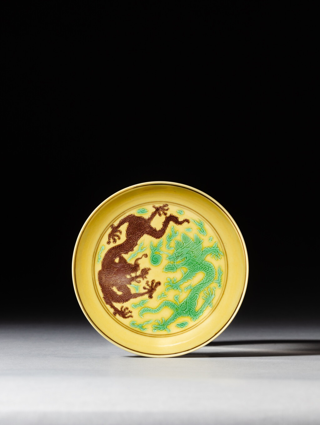 View full screen - View 1 of Lot 189. A green and aubergine enamelled yellow-ground 'dragon' dish, Mark and period of Kangxi | 清康熙 黃地紫綠彩雙龍趕珠紋盤 《大清康熙年製》款 .