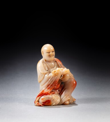 View full screen - View 1 of Lot 214. A carved 'chicken blood' soapstone figure of a Luohan, signed Yang Yuxuan, 17th century | 十七世紀 雞血石石雕羅漢坐像《玉璇》款.