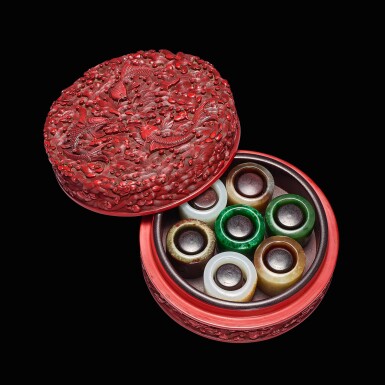 View full screen - View 1 of Lot 15. An extraordinary group of seven jade imperial archer's rings with its imperial inscribed cinnabar lacquer box and cover, Marks and period of Qianlong; the box and cover recorded to have been made in or before 1752 | 清乾隆 御製翡翠和闐玉扳指七枚 連御製詩剔紅紫檀落花流水三魚紋蓋盒 《乾隆年製》款 據錄漆盒製於乾隆十七年或更早.