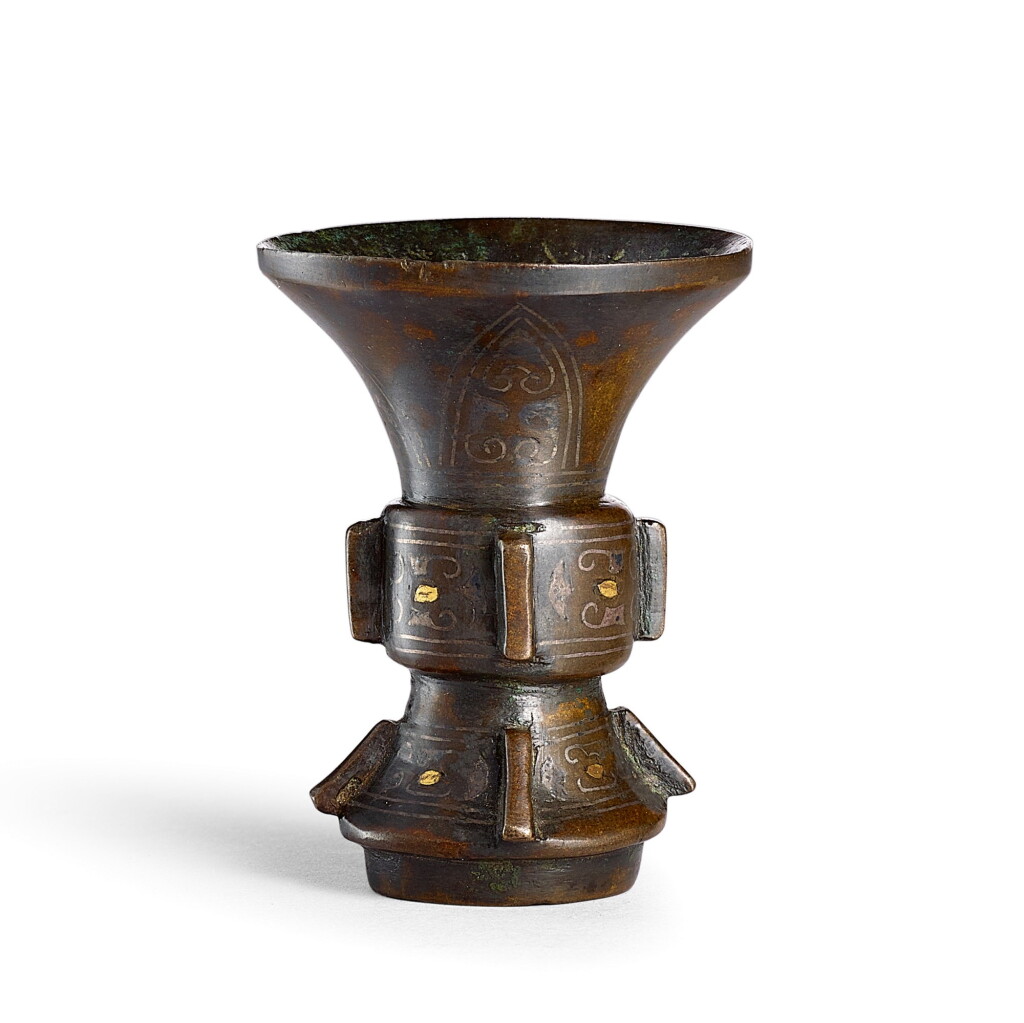 View full screen - View 1 of Lot 3667. A rare miniature gold and silver-inlaid bronze vessel, gu Song – Ming dynasty | 宋至明 銅錯金銀蕉葉卷草紋出戟袖珍型觚.