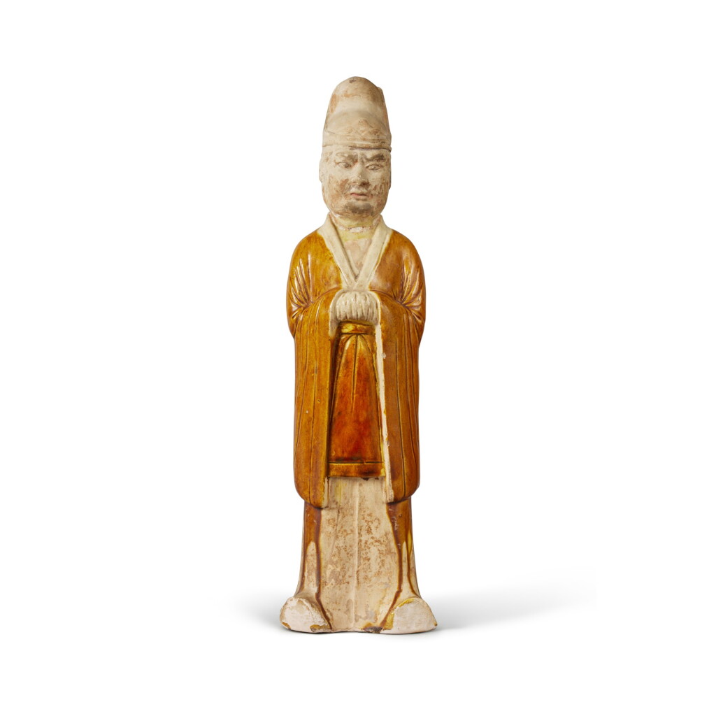 View full screen - View 1 of Lot 669. A straw- and amber-glazed pottery figure of an official, Tang dynasty | 唐 白釉褐彩文官立像.