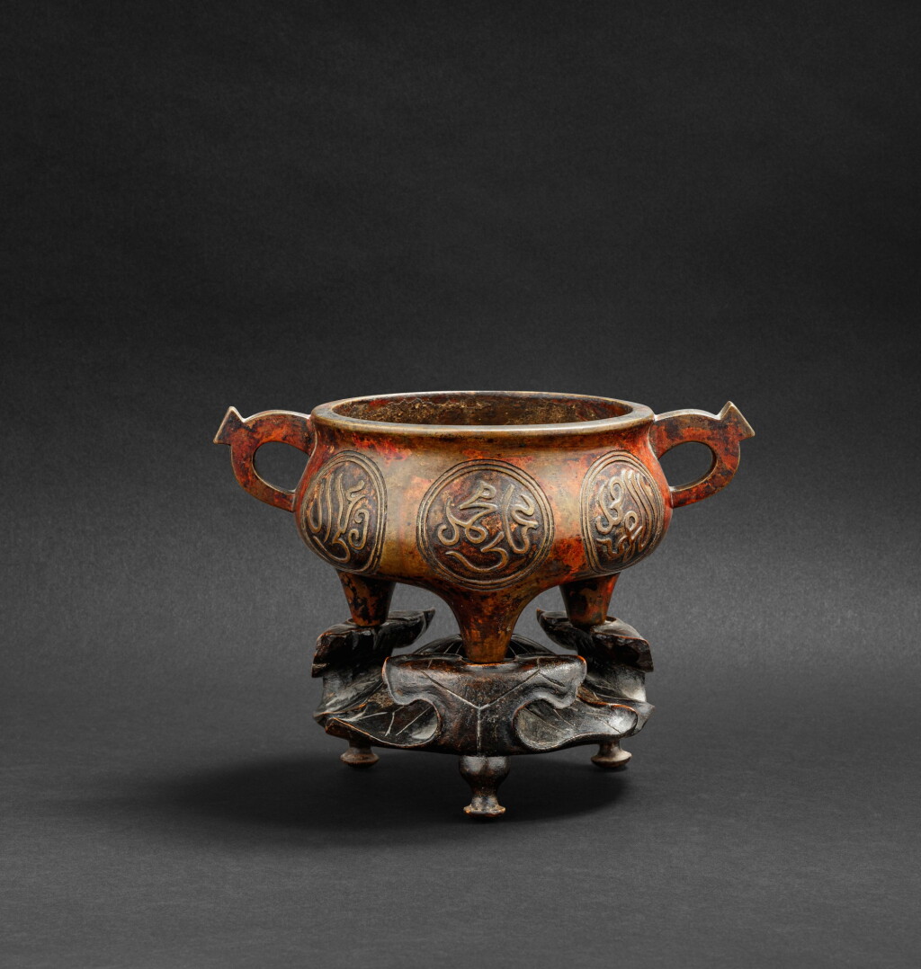 View full screen - View 1 of Lot 160. Brûle-parfum tripode en bronze avec inscriptions arabes XVIIE siècle | 十七世紀 銅阿拉伯文雙耳三足香爐 《宣德年製》仿款 | An arabic-inscribed bronze incense burner on a lotus wood stand, 17th century.